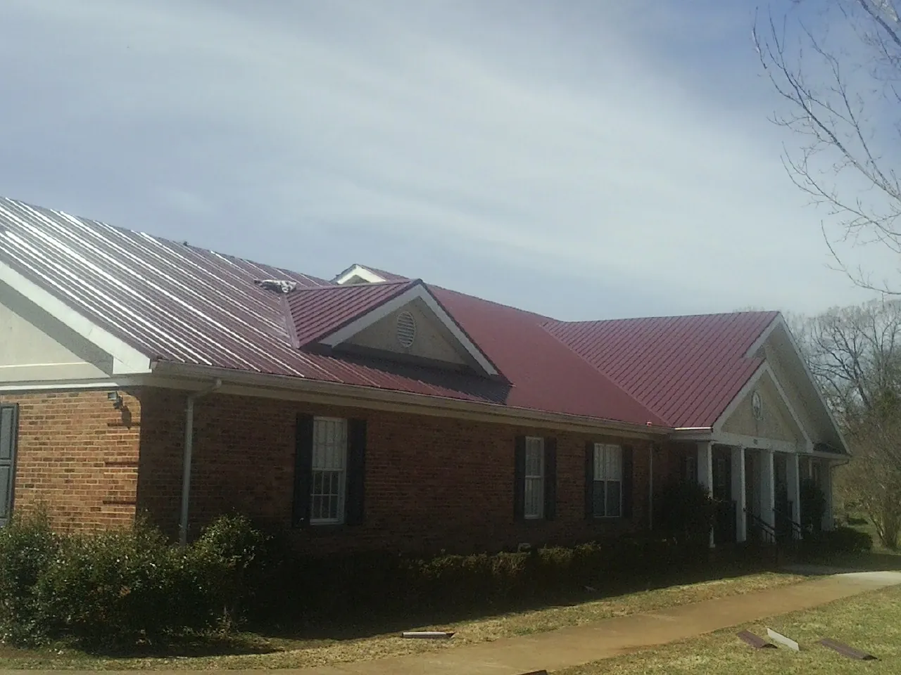 Red metal roof with gabled entries on a long brick building, from a Hail Damage Roof Repair job in Bristol