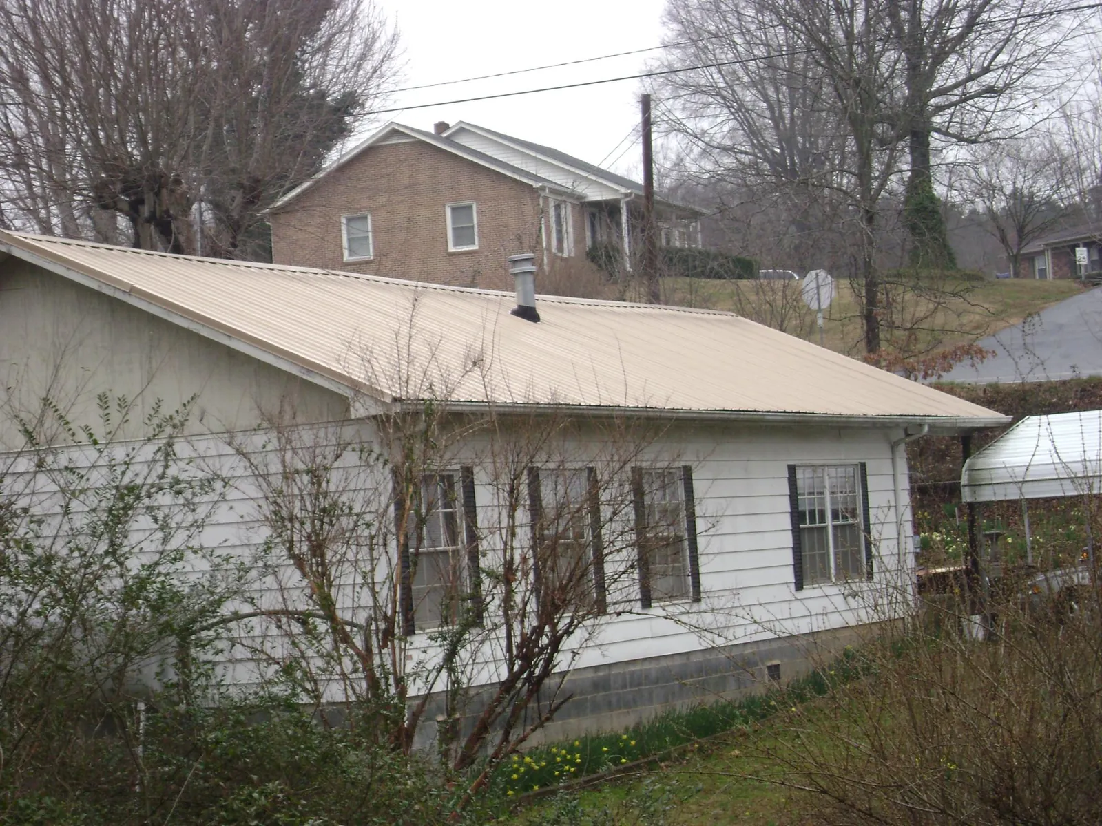 Tan metal roof on a white sided house set into a hillside — Commercial Roofing by Roofing Brothers in Bristol